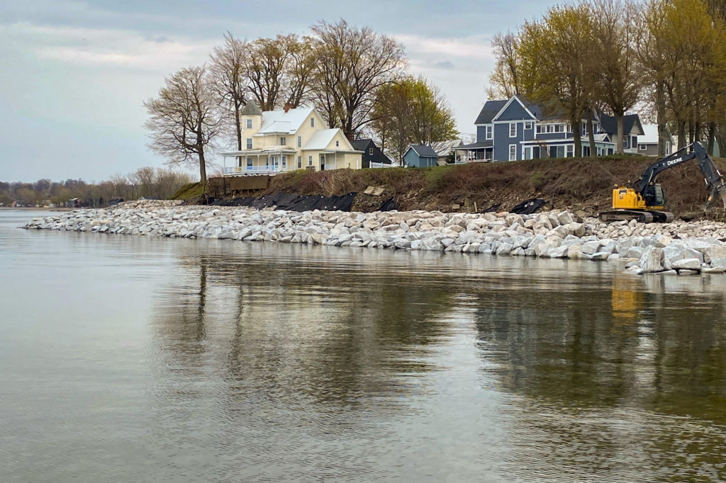 Victorian and farm-style homes next to a wall of seawall rock with a view of water